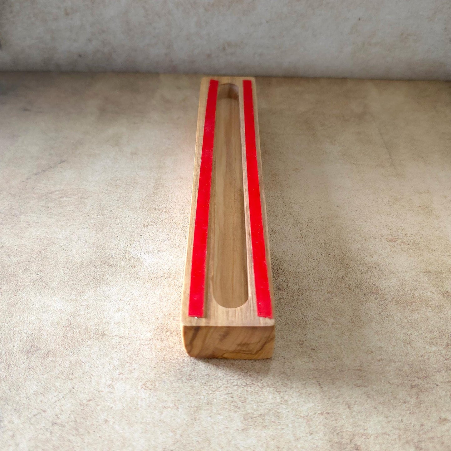 A wooden object with red tape on it, placed on a beige surface.